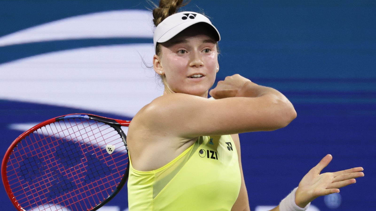 Tennis player in visor and neon shirt swings racket during a match
