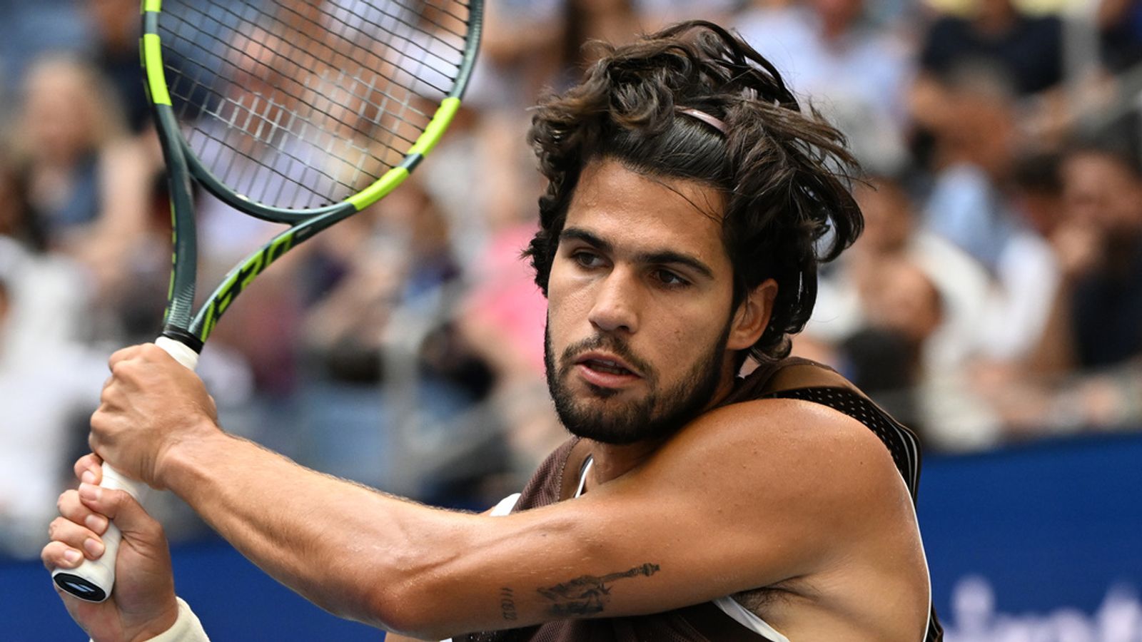 Male tennis player swings a racket during a match with spectators blurred behind him
