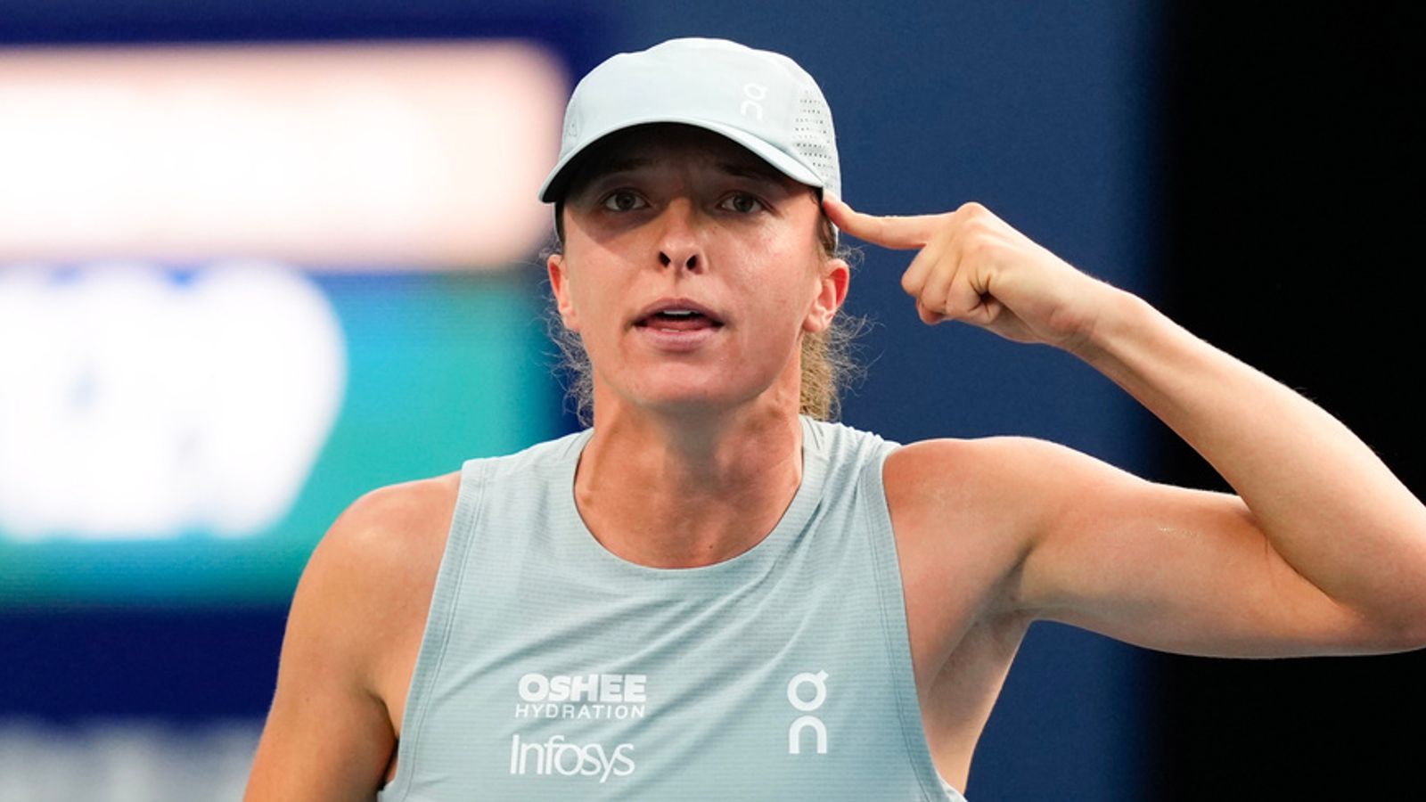Female tennis player in cap and sleeveless top gestures toward her temple during a match