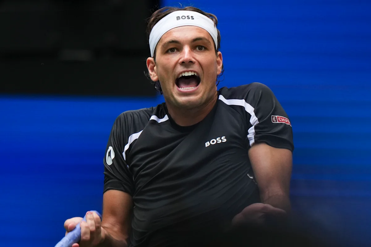 Tennis player shouting in a black shirt and white headband against a blue backdrop