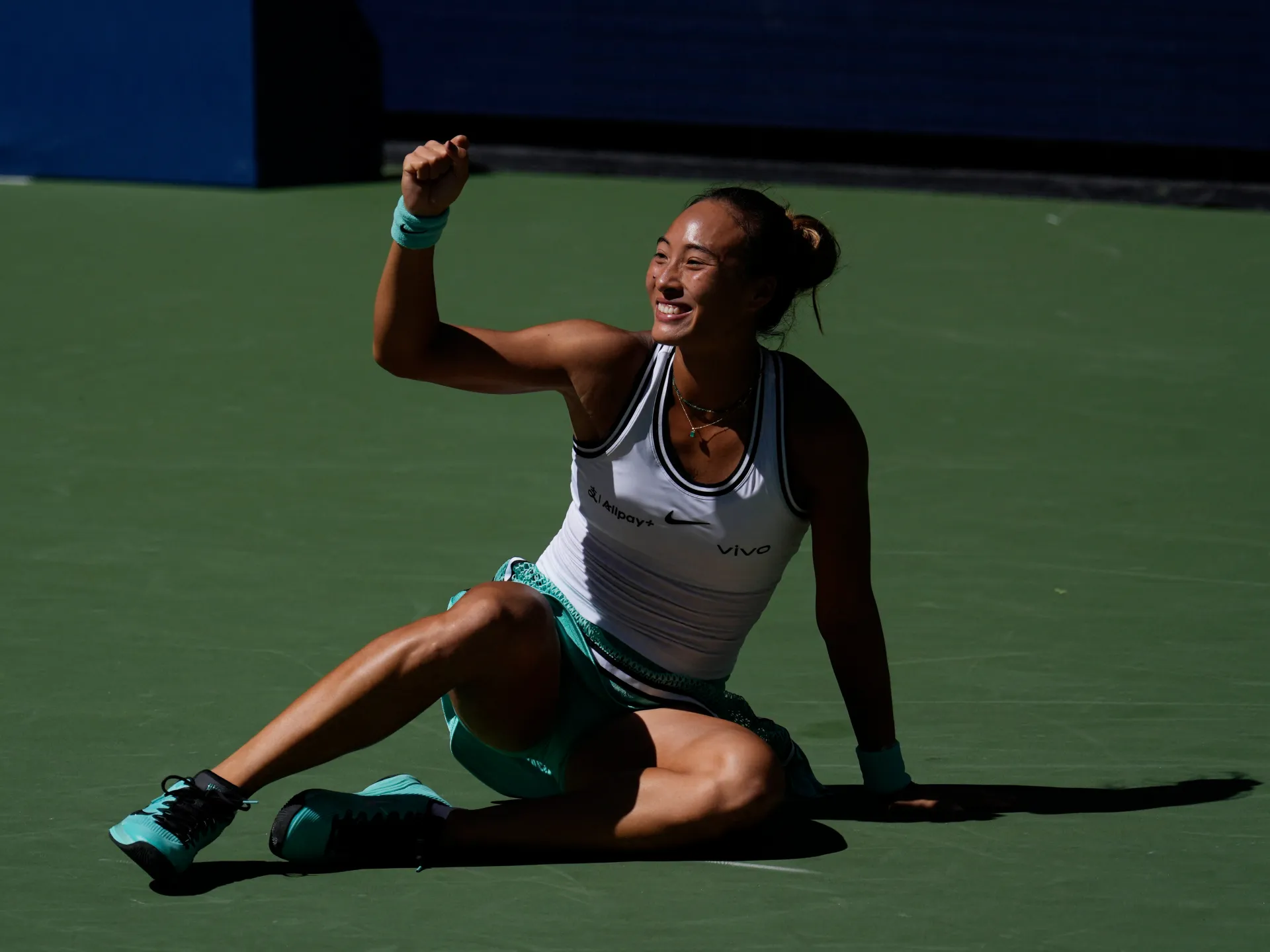 Tennis player seated on court, raising a fist and smiling after a match.