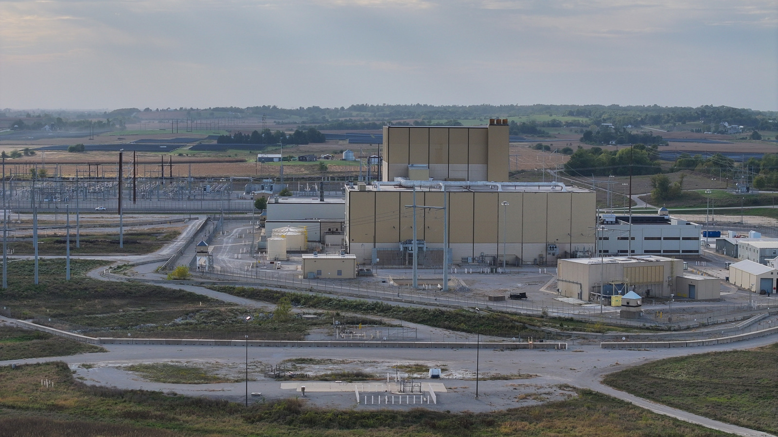 Large industrial power facility with electrical substations and farmland visible in the background