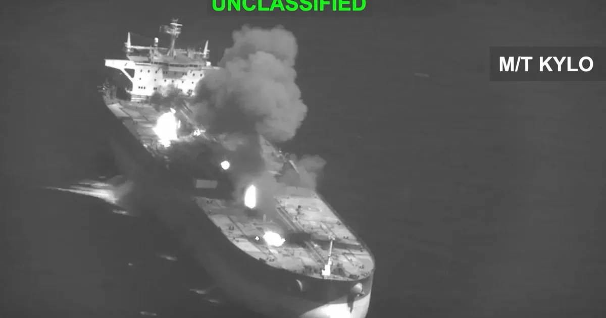 Aerial grayscale image of a large tanker burning, with flames and thick smoke rising from its deck.