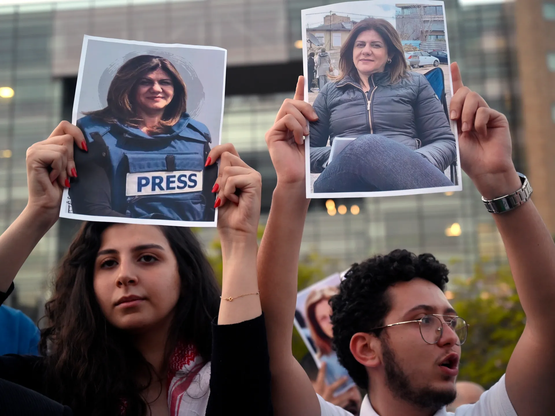 Protesters hold photographs of a woman, including one showing her in a press vest.
