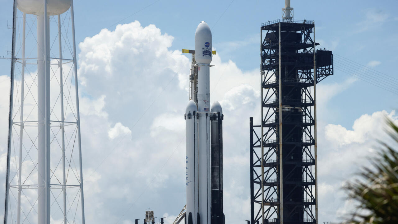 Rocket standing vertically beside a launch tower beneath a partly cloudy blue sky
