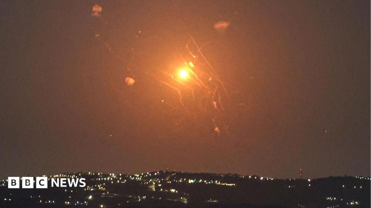 Bright orange flash illuminates the night sky above scattered city lights