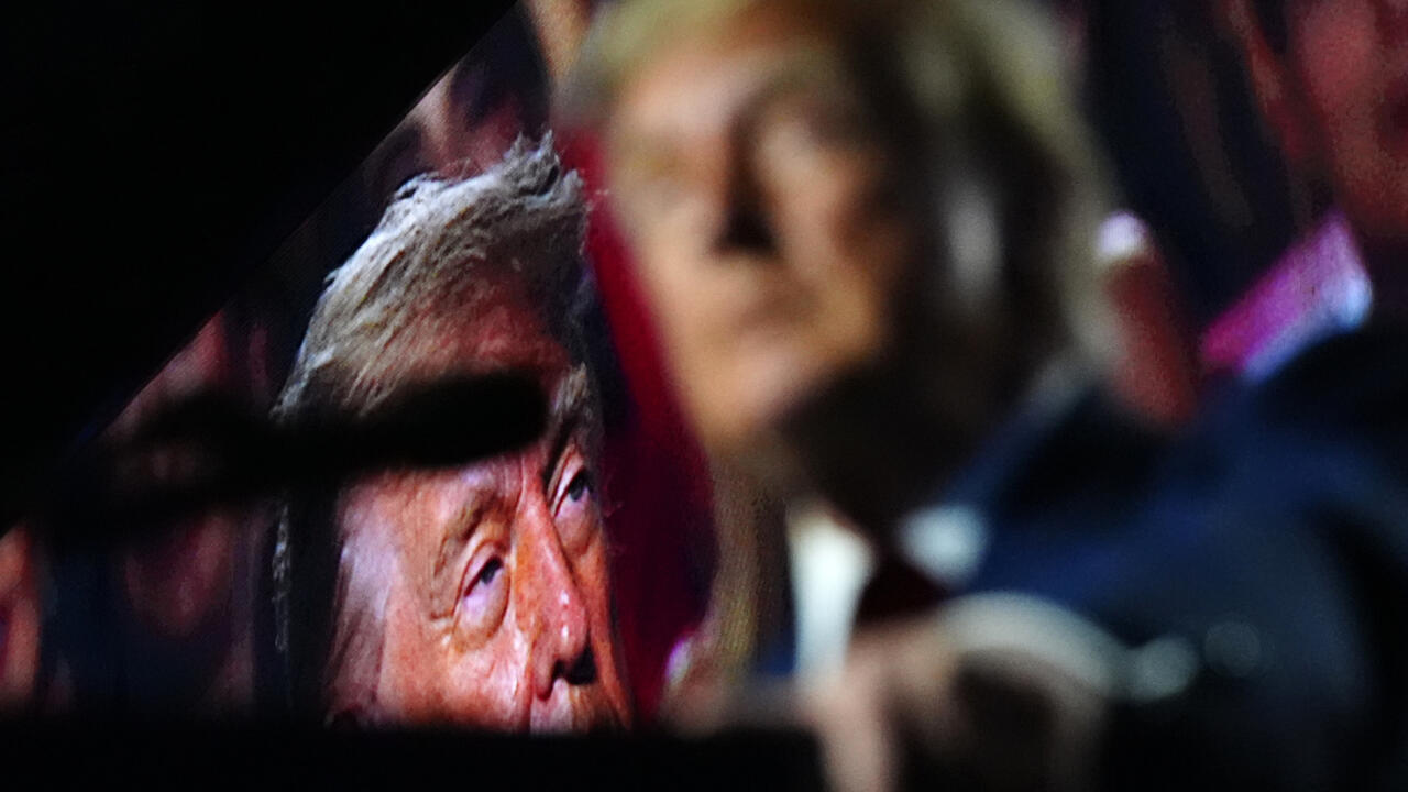 A close-up of two people, one wearing a dark cap, in a dimly lit setting.