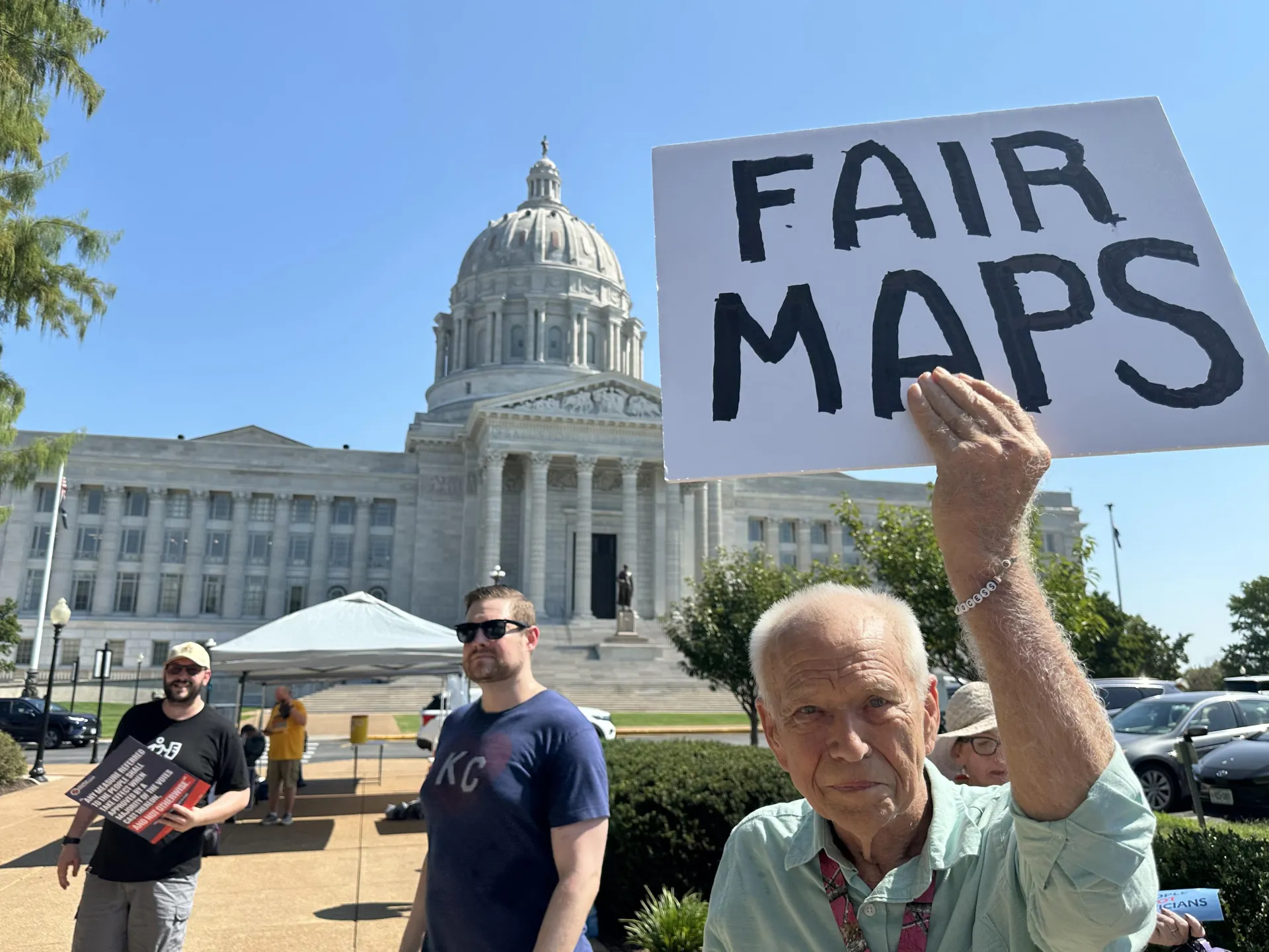 Demonstrator holds a handwritten “FAIR MAPS” sign outside a domed government building.