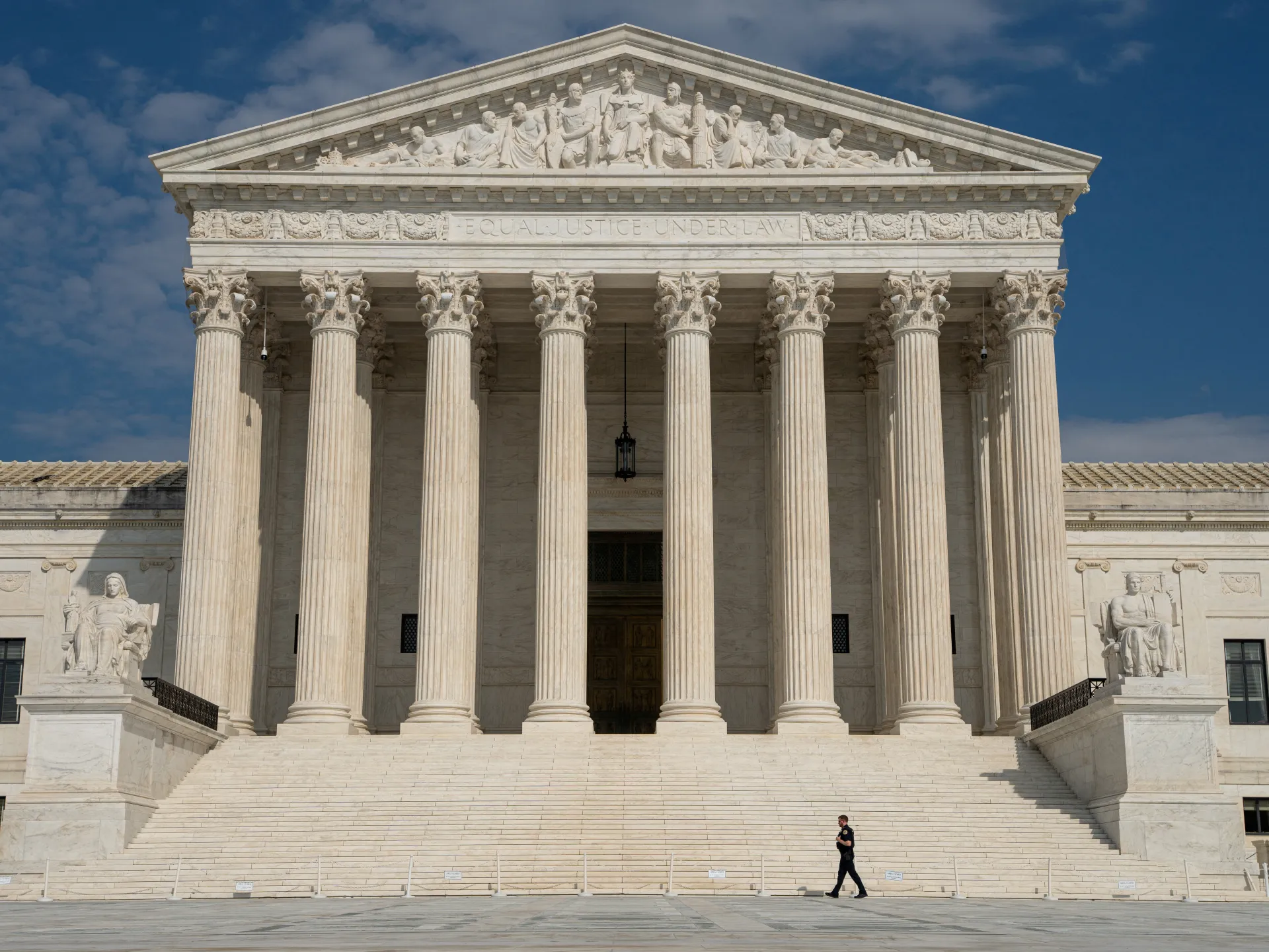 Front facade of a neoclassical courthouse with columns, sculpted figures, steps, and a person walking outside