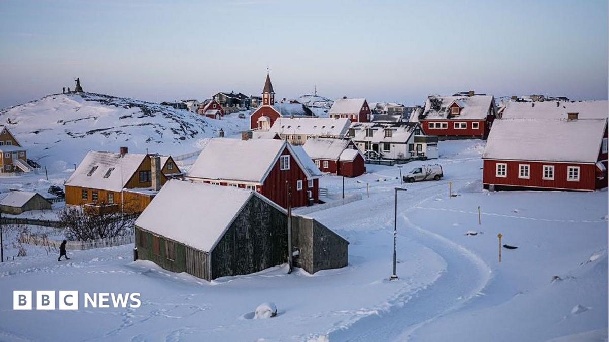 Snow-covered coastal settlement with colorful houses and a church beneath a pale winter sky.