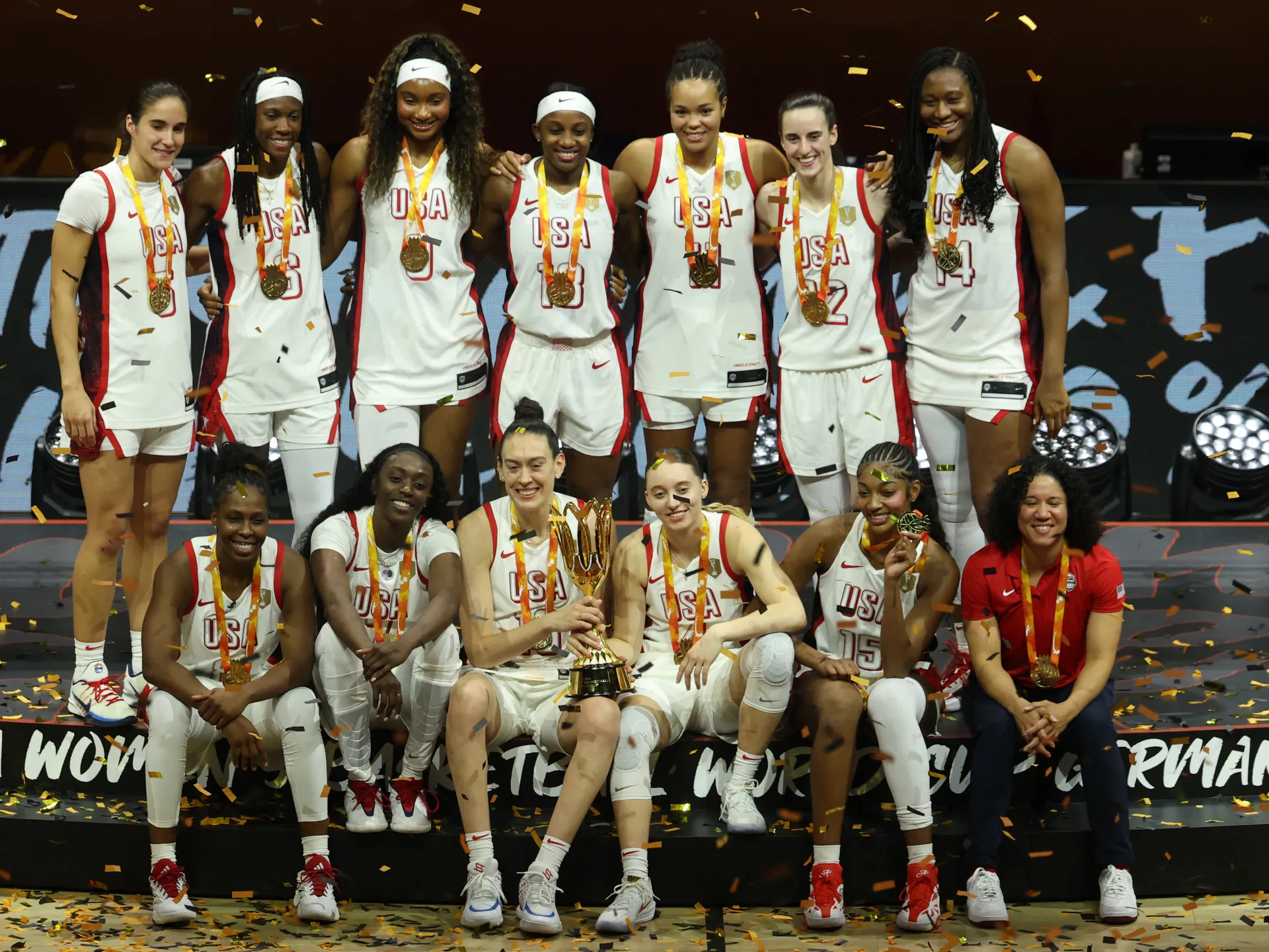 USA women’s basketball team poses with medals and trophy amid falling confetti.