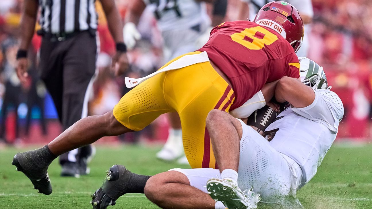 USC player in cardinal and gold tackles a white-uniformed quarterback during a football game.