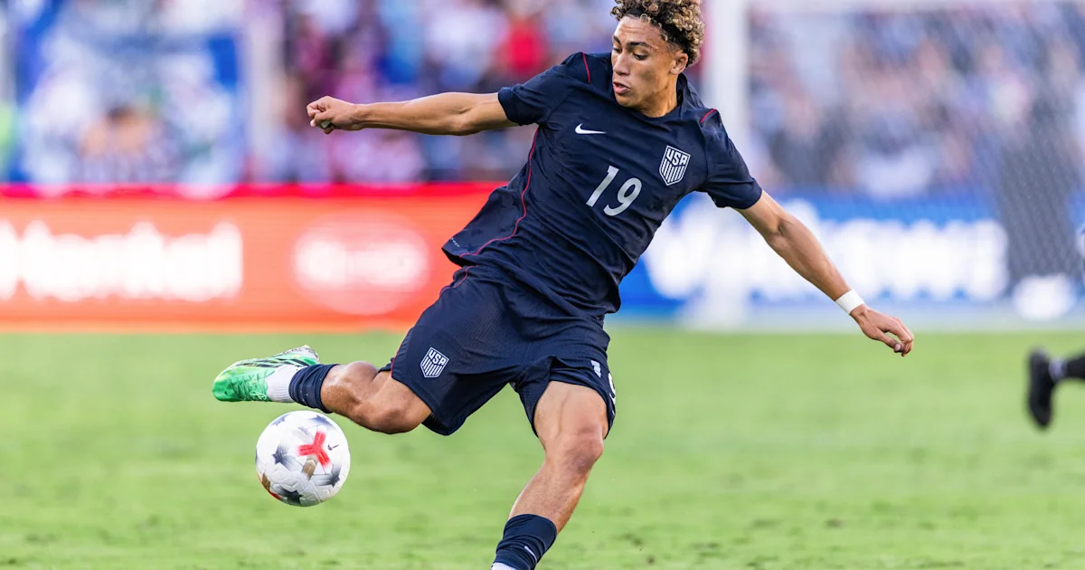USA player in a navy uniform kicks a soccer ball during a match.
