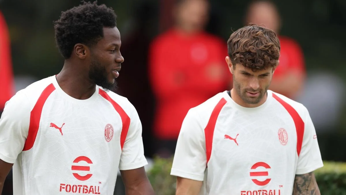 Two soccer players in white and red AC Milan training shirts stand together during practice.