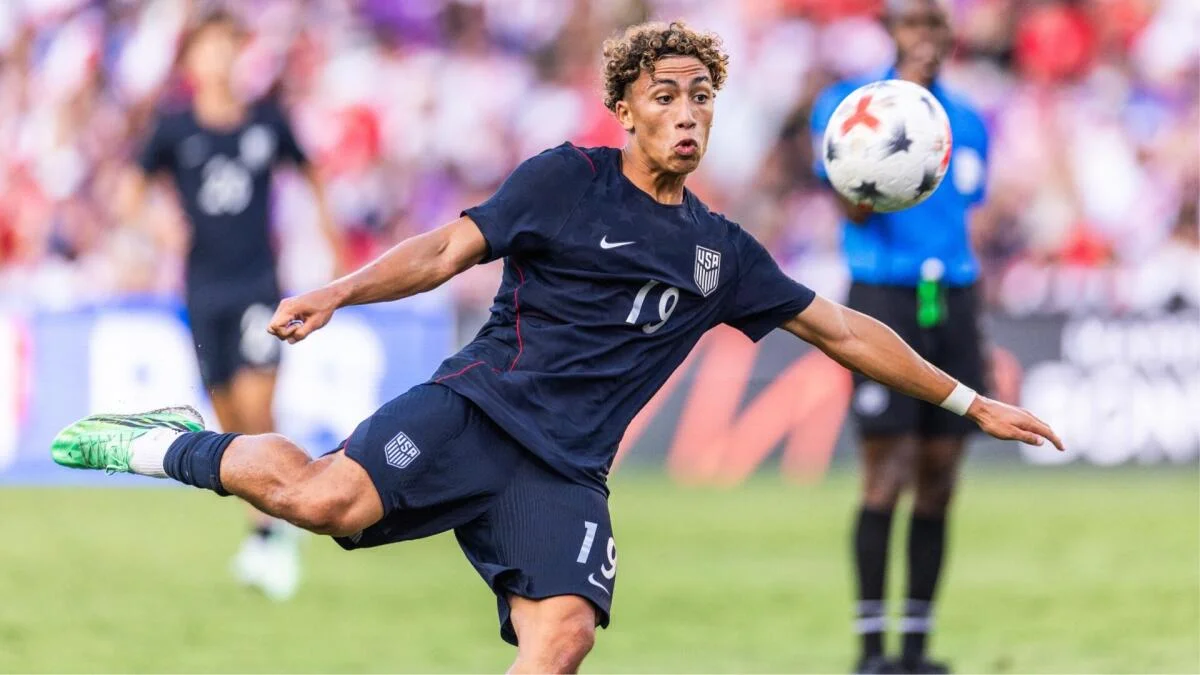 USA player in a navy kit kicks toward a ball during a soccer match.