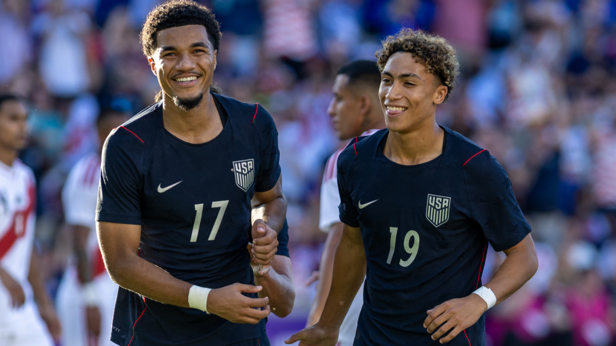 Two smiling U.S. players in dark jerseys walk together on the field during a match.