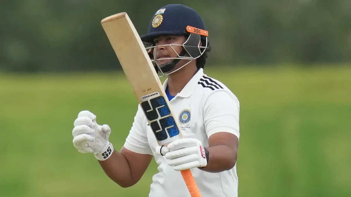 Young cricketer in helmet and white uniform holds a bat on a grassy field