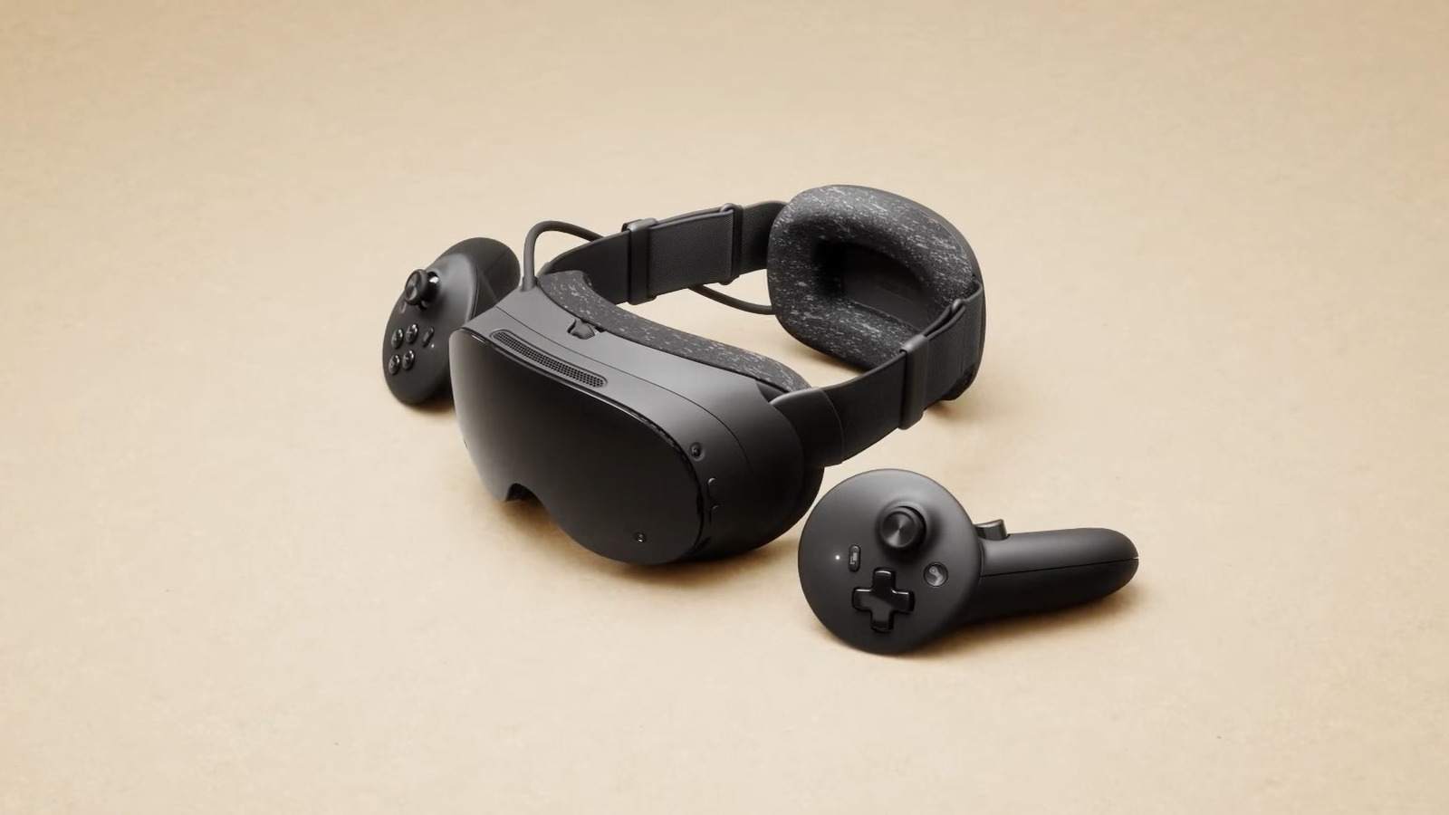 Black VR headset with padded strap and two handheld controllers on a beige surface