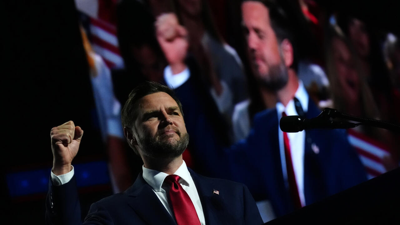Man in suit raises a fist while speaking at a microphone before a large projected image.