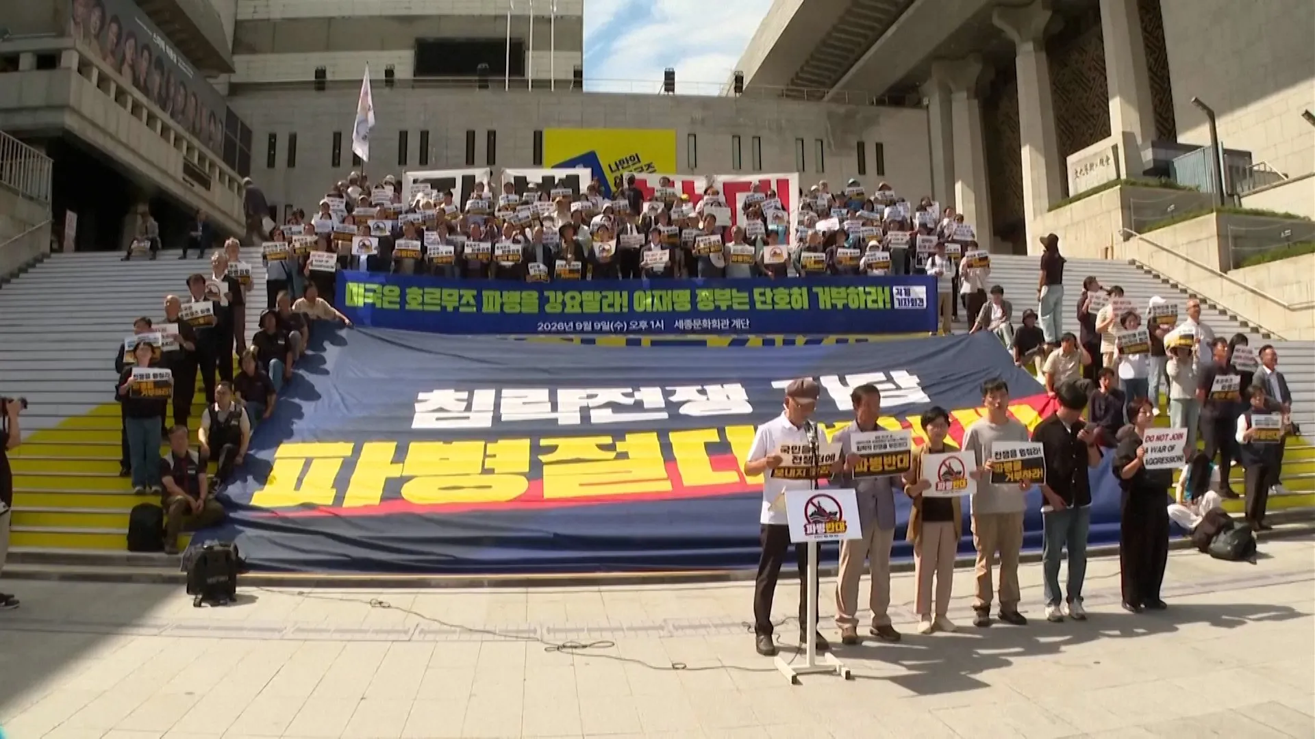 Large group of protesters holding signs and a banner outside a modern building