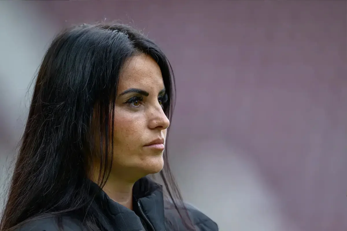 Woman with long dark hair in profile, wearing a dark jacket against a blurred background.