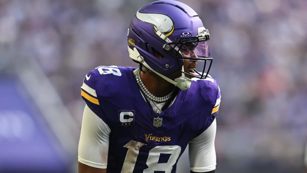 Football player in a purple Vikings uniform and helmet looks to the side on the field.