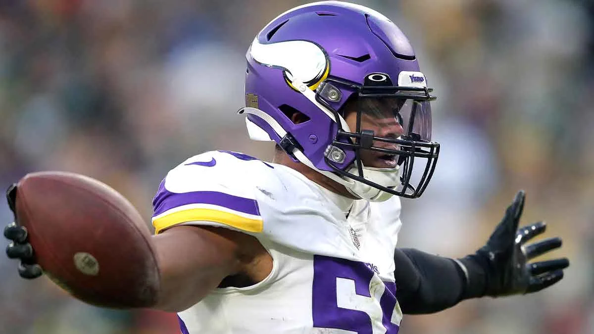 Minnesota Vikings football player in purple helmet and white jersey extending a football during play