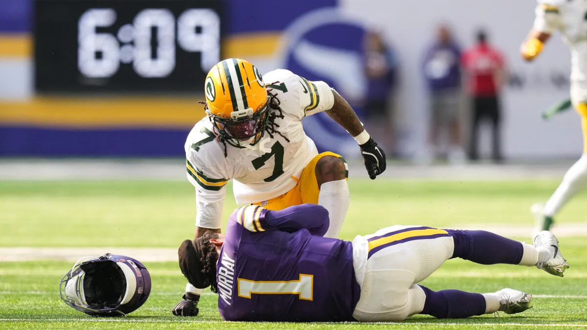 Football players in Packers and Vikings uniforms collide during a game on a sunlit field