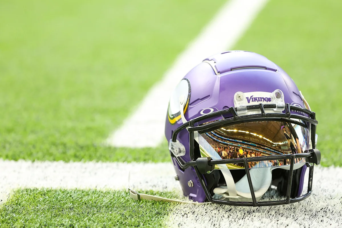 Purple Vikings football helmet resting on white field markings and green turf