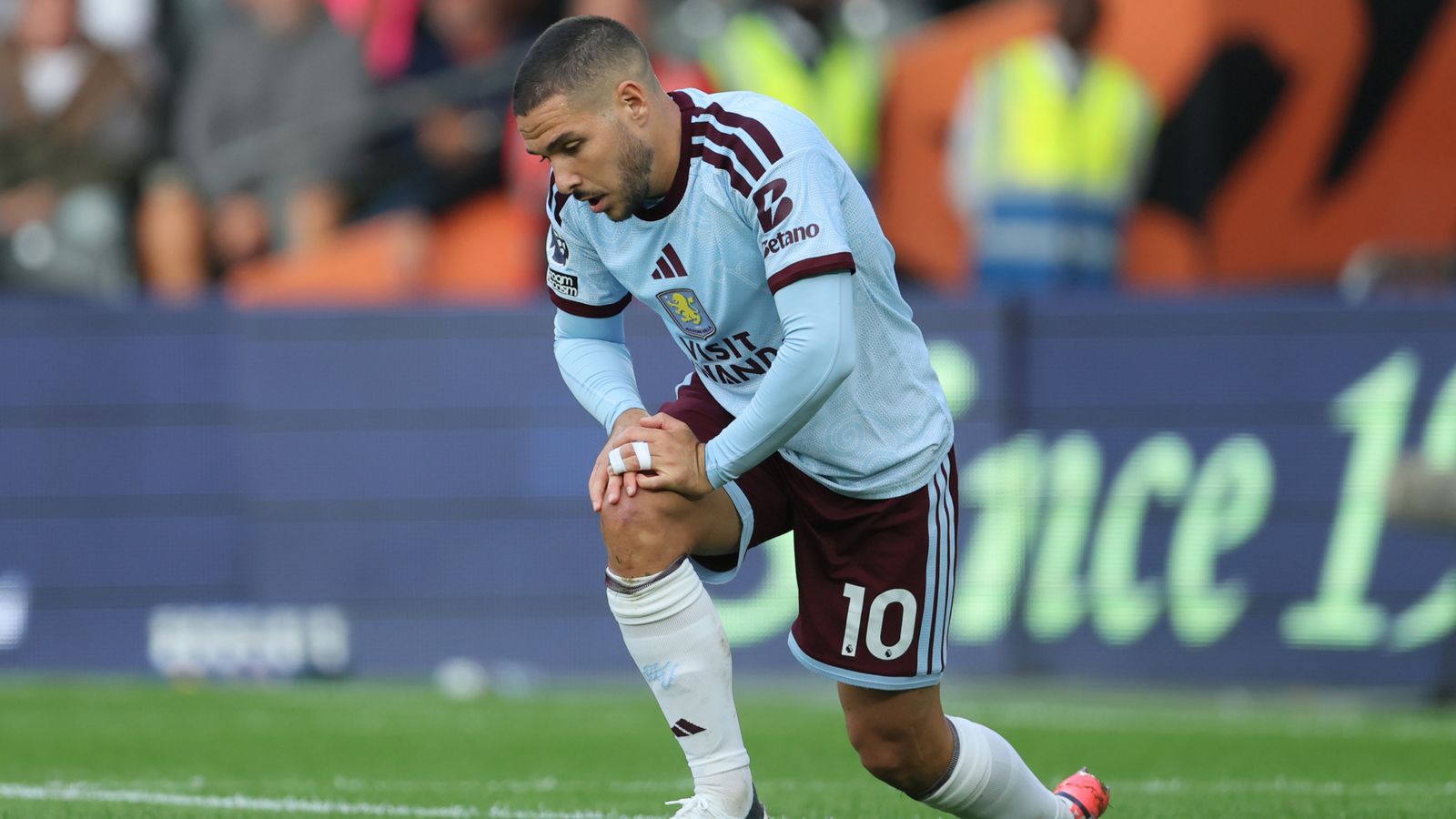 Aston Villa footballer crouches on the pitch, holding his knee during a match.