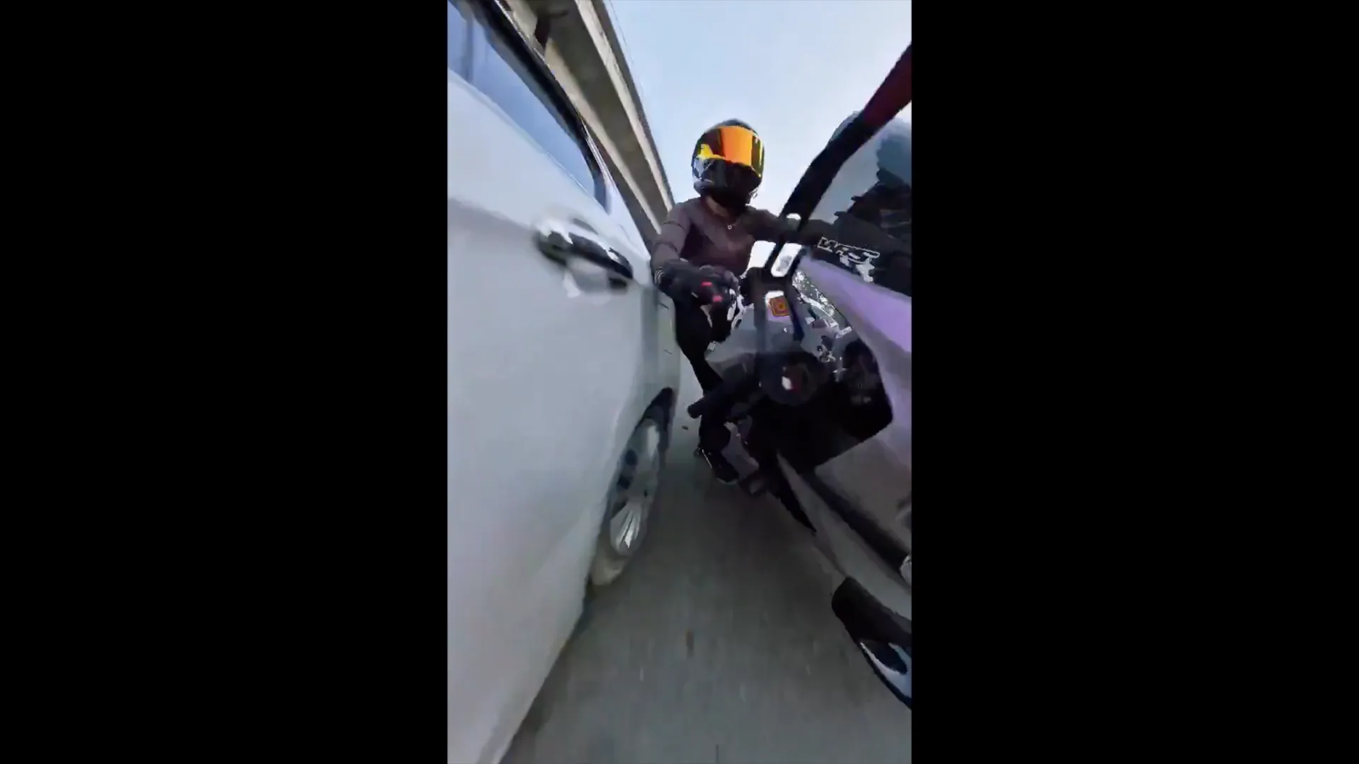 Helmeted motorcyclist rides between a white car and another vehicle on a roadway.