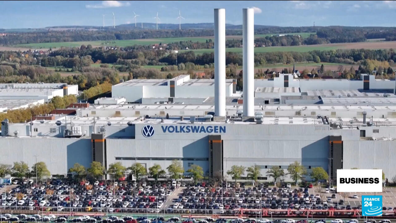 Aerial view of Volkswagen factory with smokestacks, surrounding countryside, and rows of parked cars.