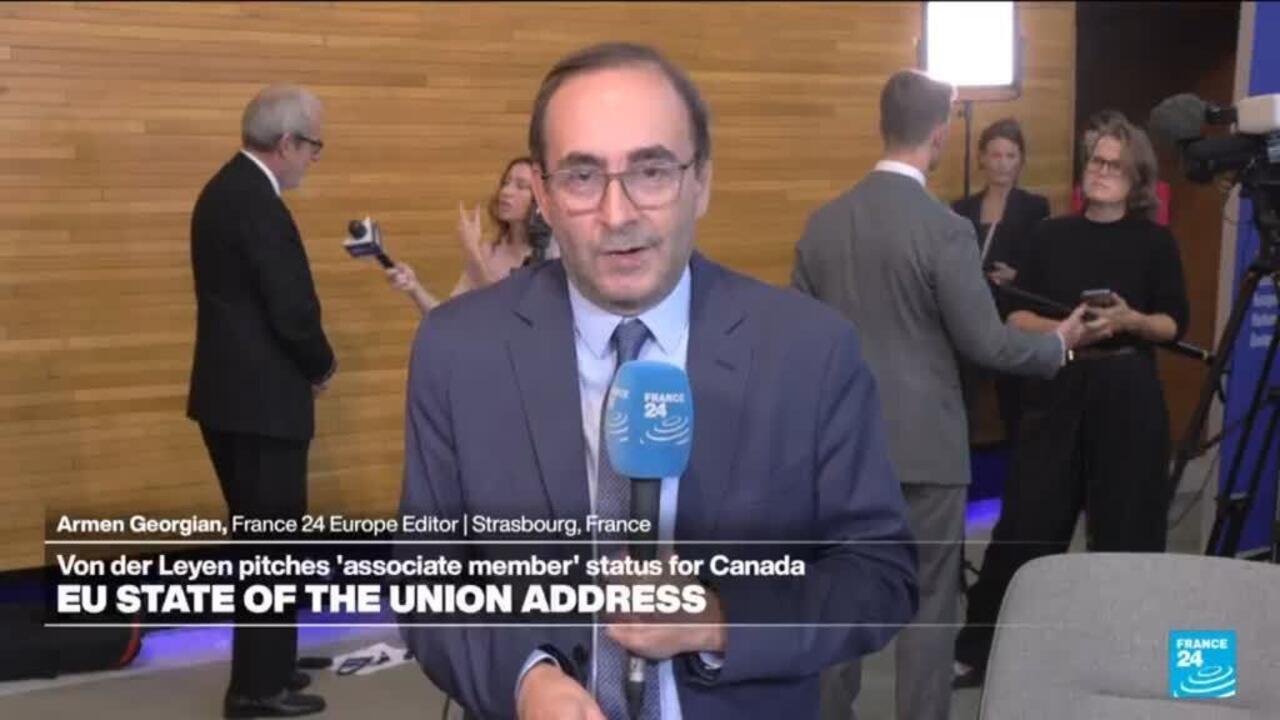 Man speaking into a France 24 microphone during a televised interview in an indoor venue.