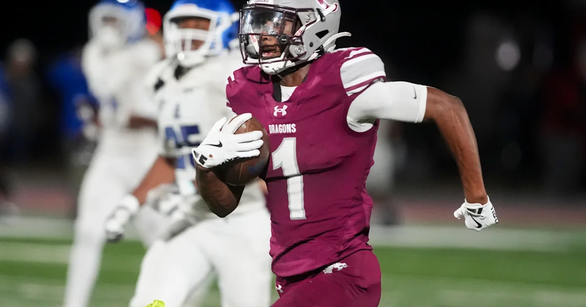 Football player in a maroon number 1 jersey runs with the ball as opponents pursue.