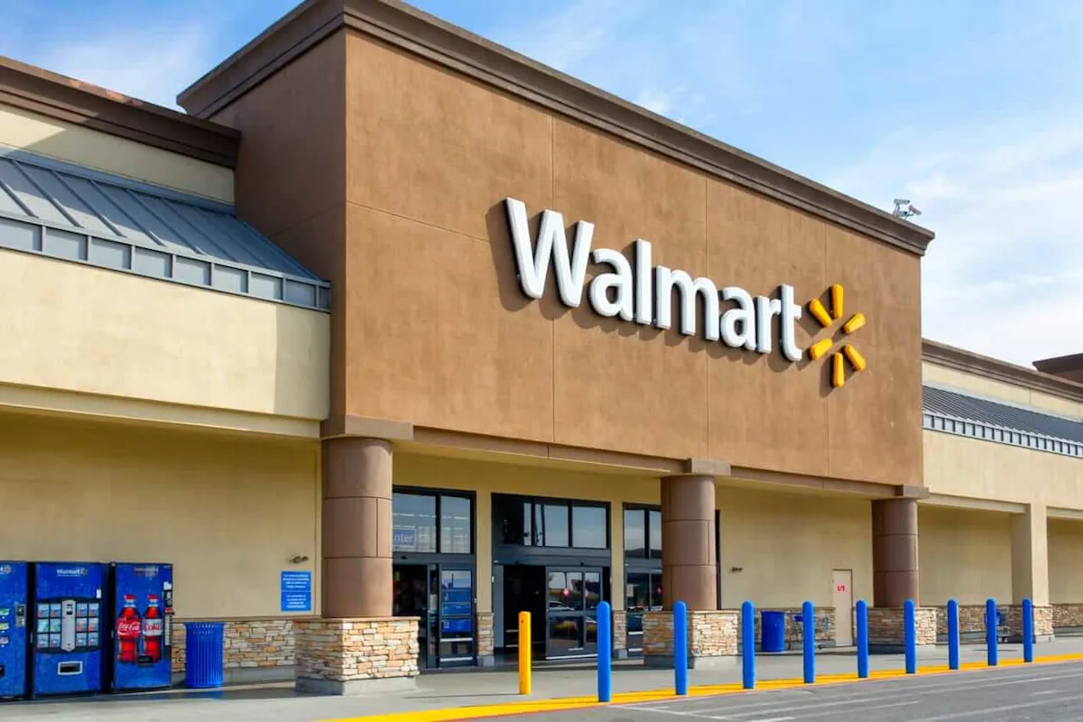 Walmart storefront with large logo, entrance doors, blue bollards, vending machines, and clear sky