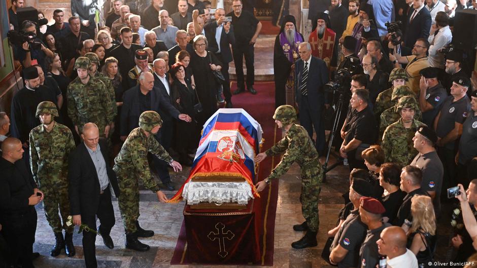 Soldiers carry a Serbian-flag-draped coffin through a crowded church surrounded by mourners.