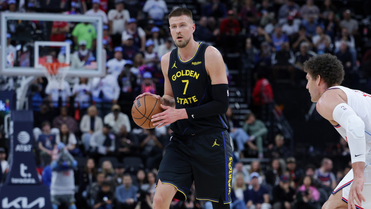 Basketball player in a dark number seven uniform holds the ball as an opponent crouches nearby.