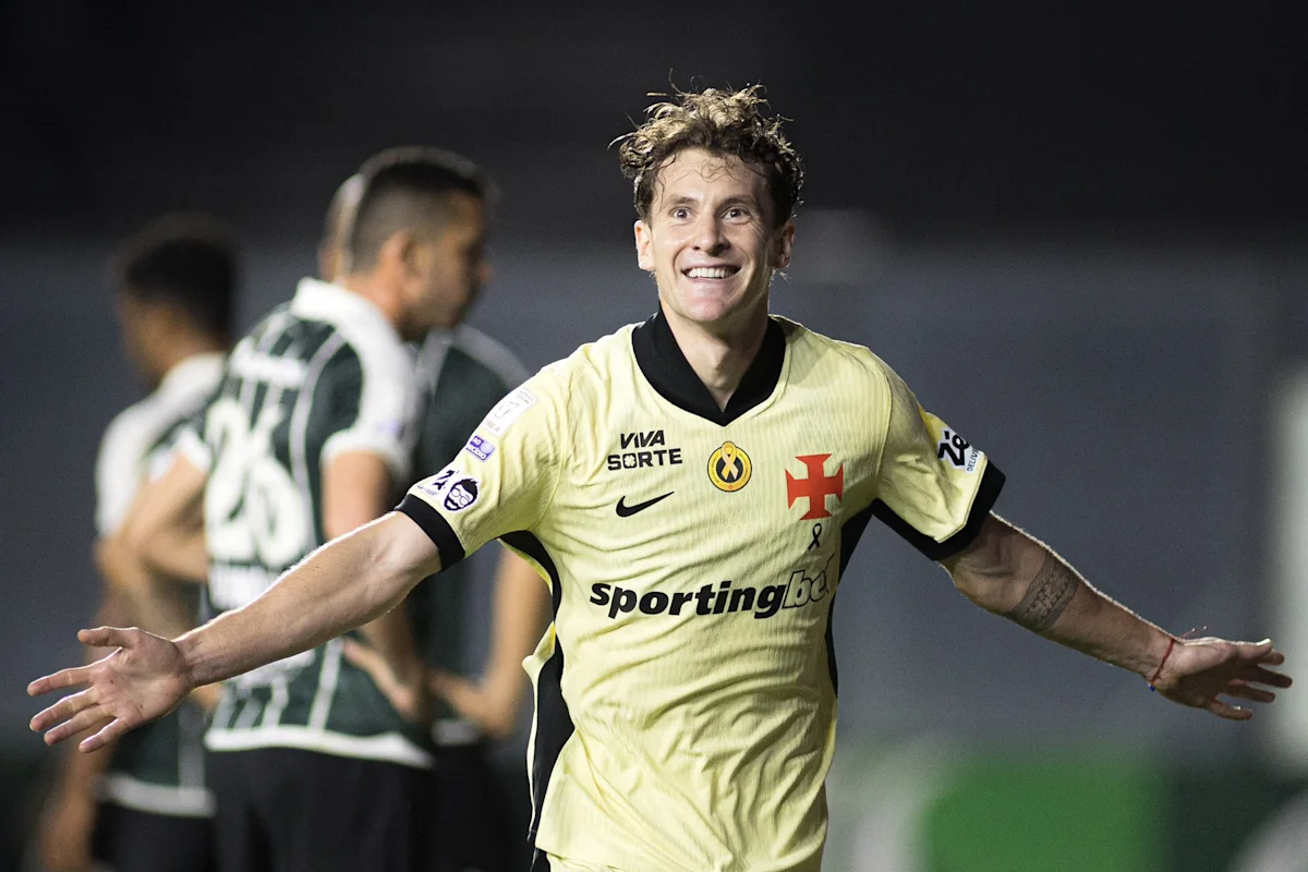 Smiling footballer in yellow jersey celebrates with arms outstretched during a night match.