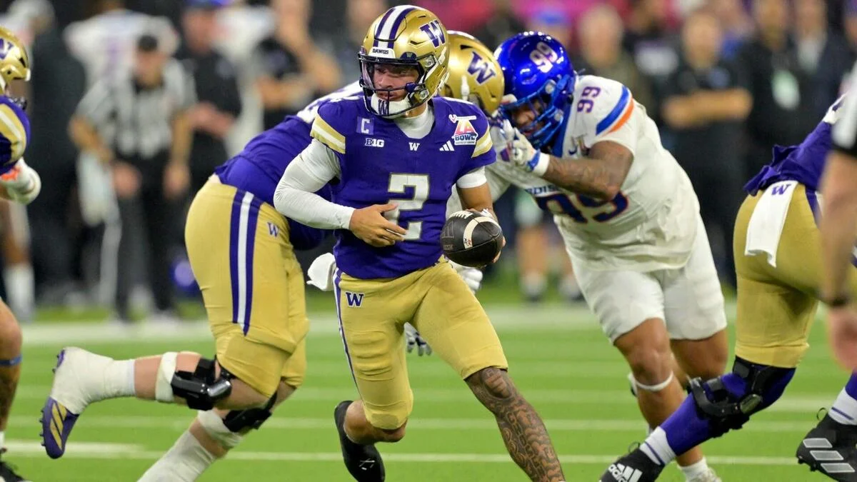 Washington quarterback runs with football as defenders pursue during a college football game