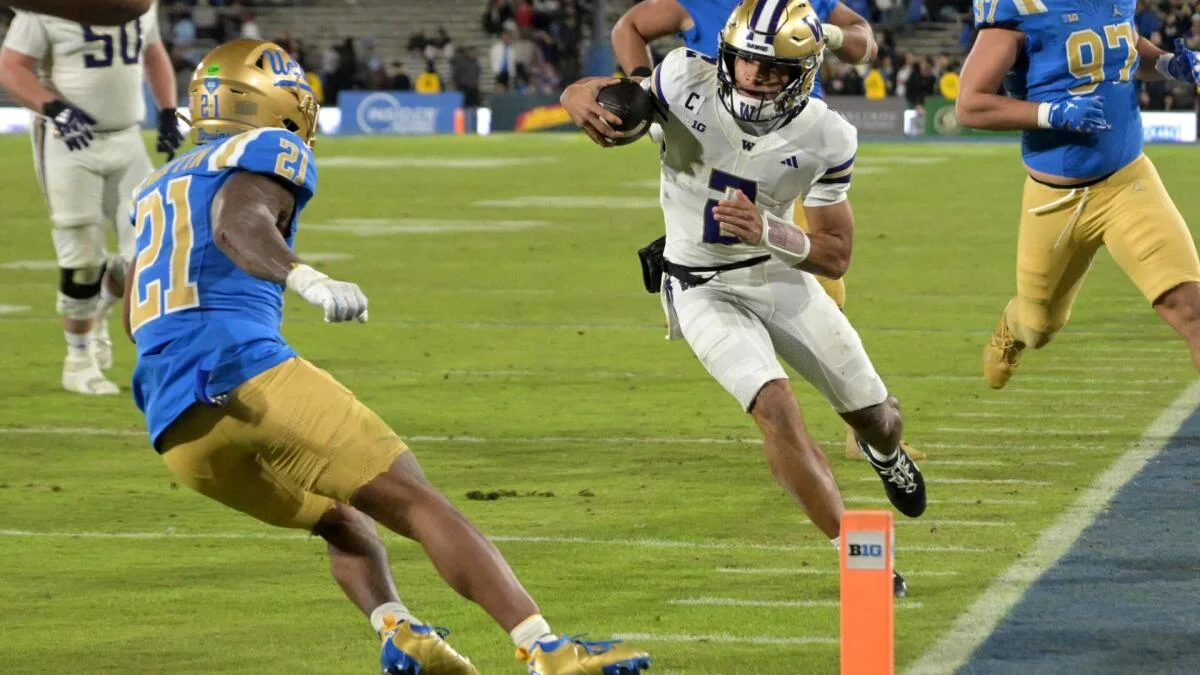 Washington football player runs with the ball near the sideline as defenders pursue.