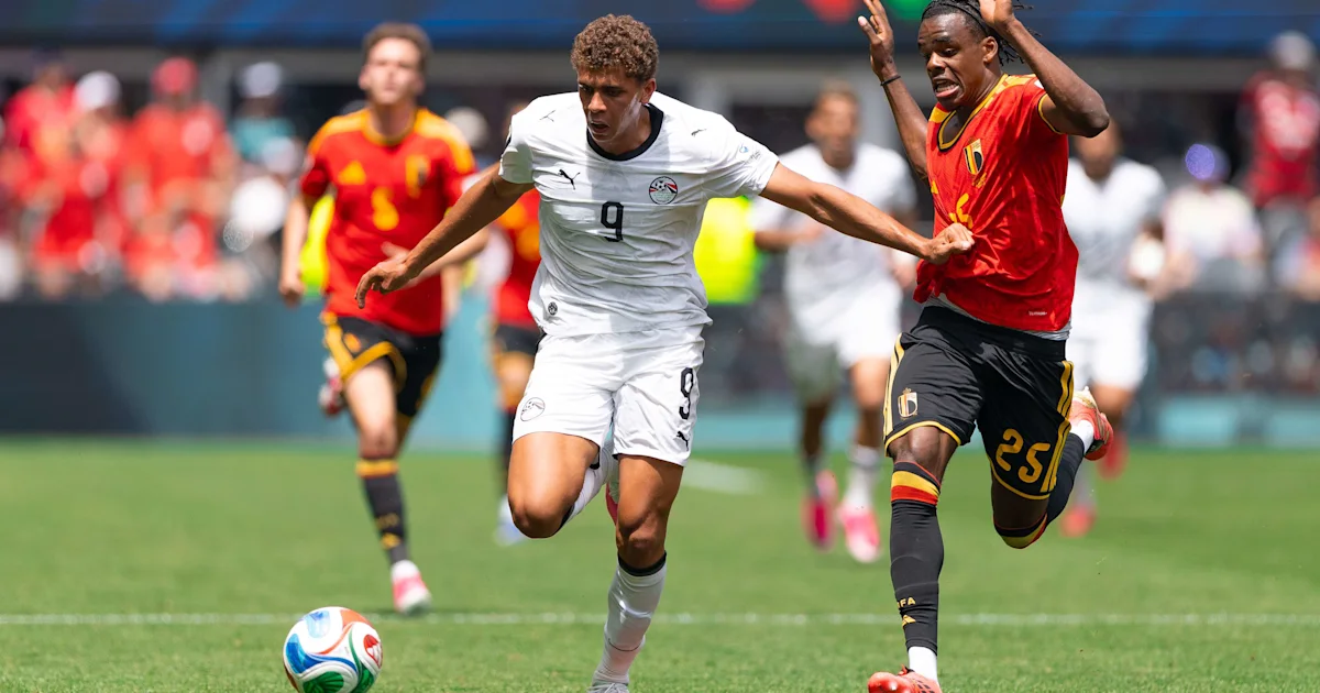 A player in Egypt’s white kit runs beside a Belgium player in red during a soccer match.