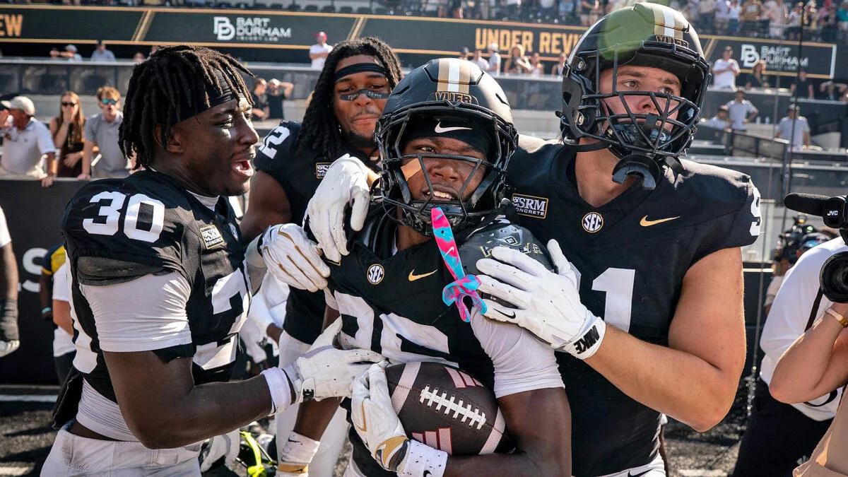 Vanderbilt football players celebrate as a helmeted teammate holds the football near the end zone.