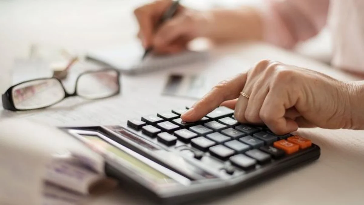 Close-up of hands using a calculator beside eyeglasses and paperwork on a desk