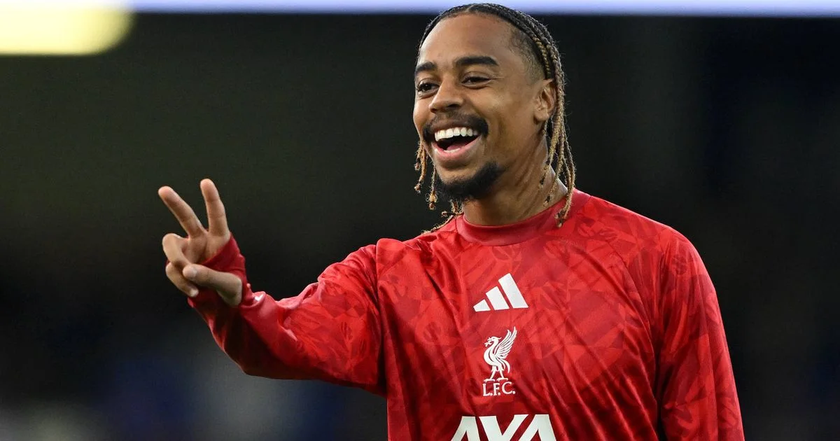 Smiling footballer in a red Liverpool training shirt raises two fingers during a public appearance.