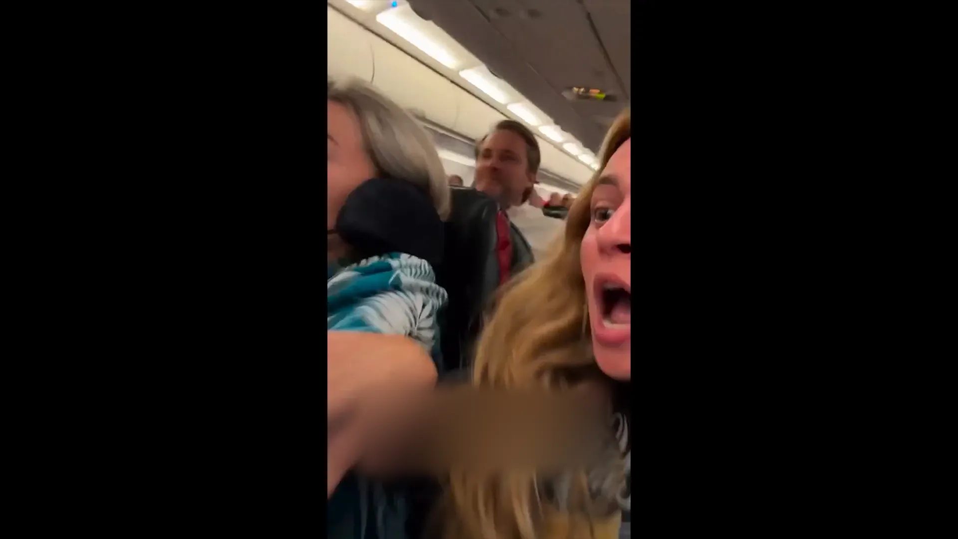 Passengers react as a uniformed crew member moves through an airplane cabin during turbulence.