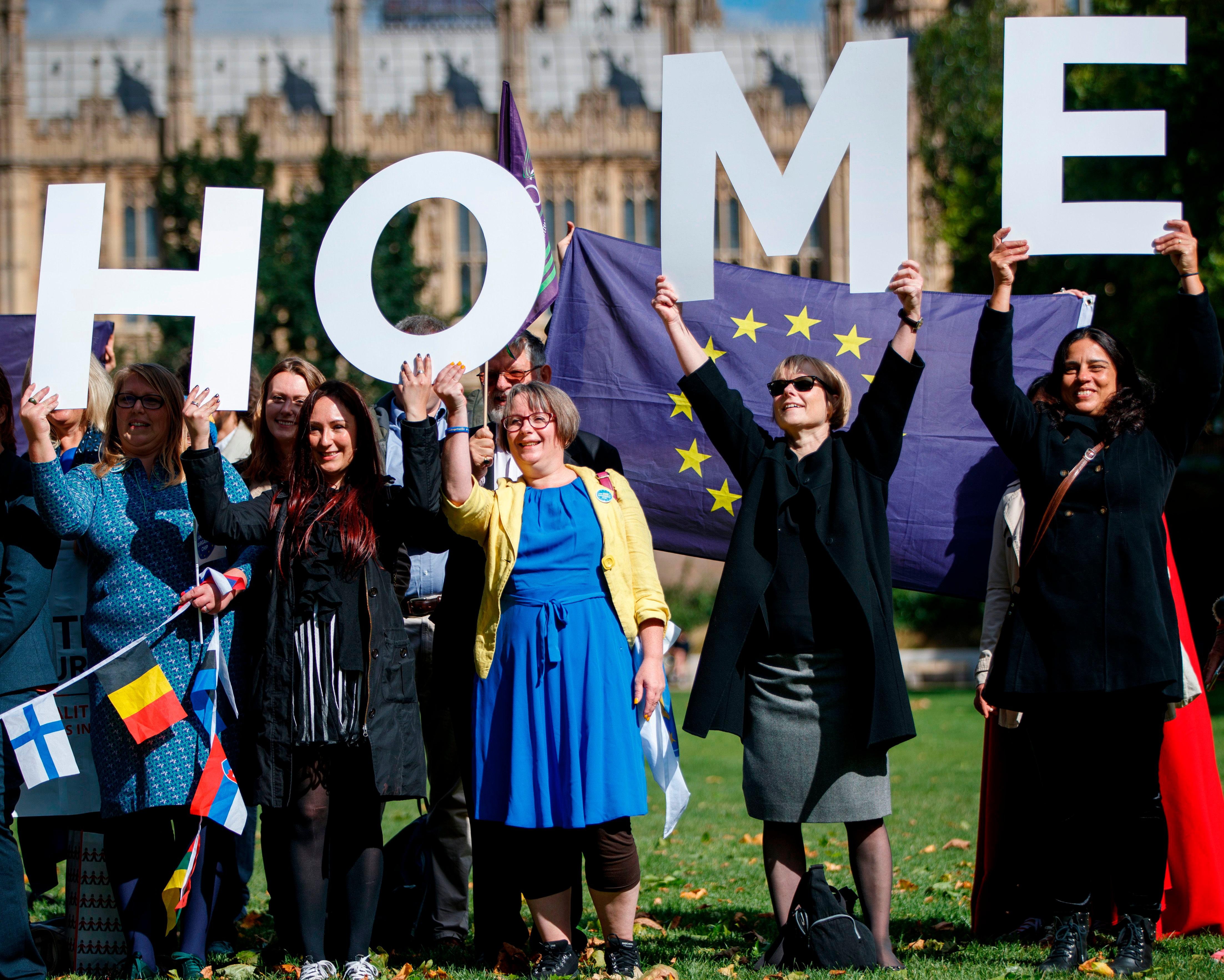 People hold large white letters spelling “HOME” above a crowd with an EU flag.