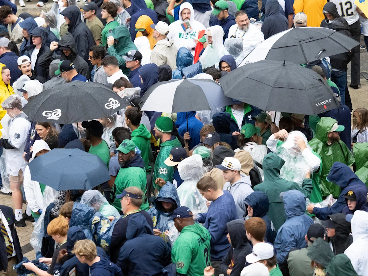 Crowd of Notre Dame fans in rain ponchos and under umbrellas during wet conditions