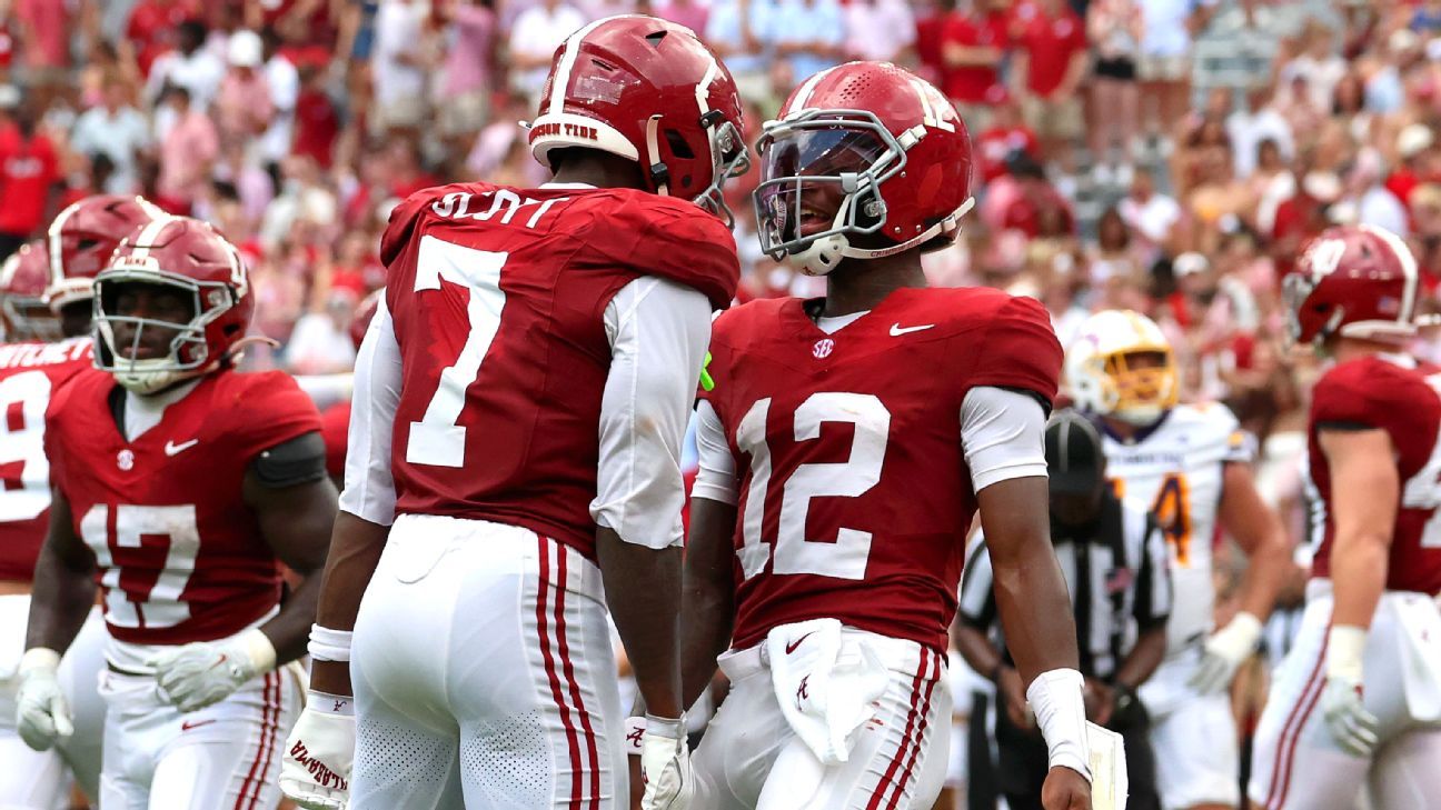 Two crimson-clad football players face each other on the field during a game.