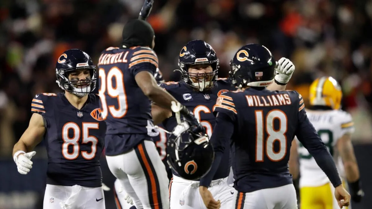 Chicago Bears players celebrate on the field as a Green Bay Packers player stands in the background.