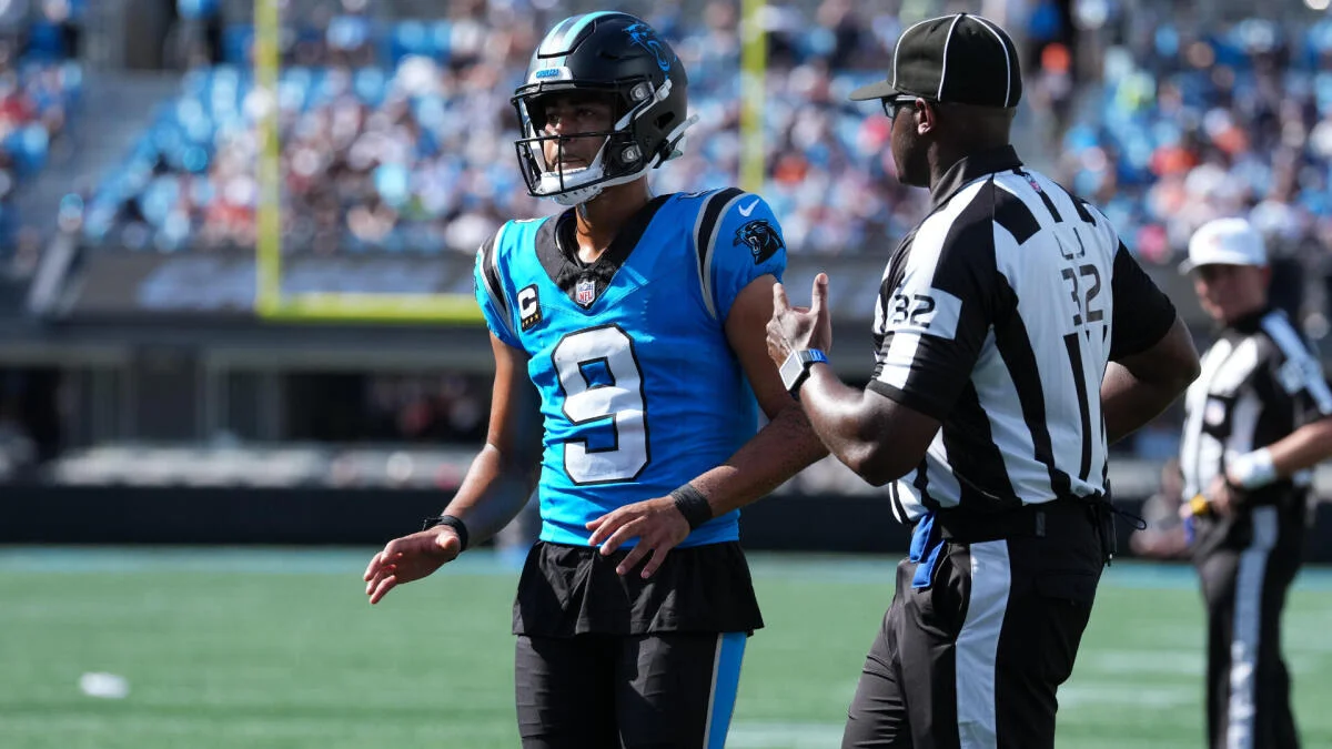 Football quarterback in blue jersey talks with a referee during a game